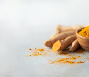 Turmeric powder in wooden bowl and fresh turmeric root on grey concrete background.